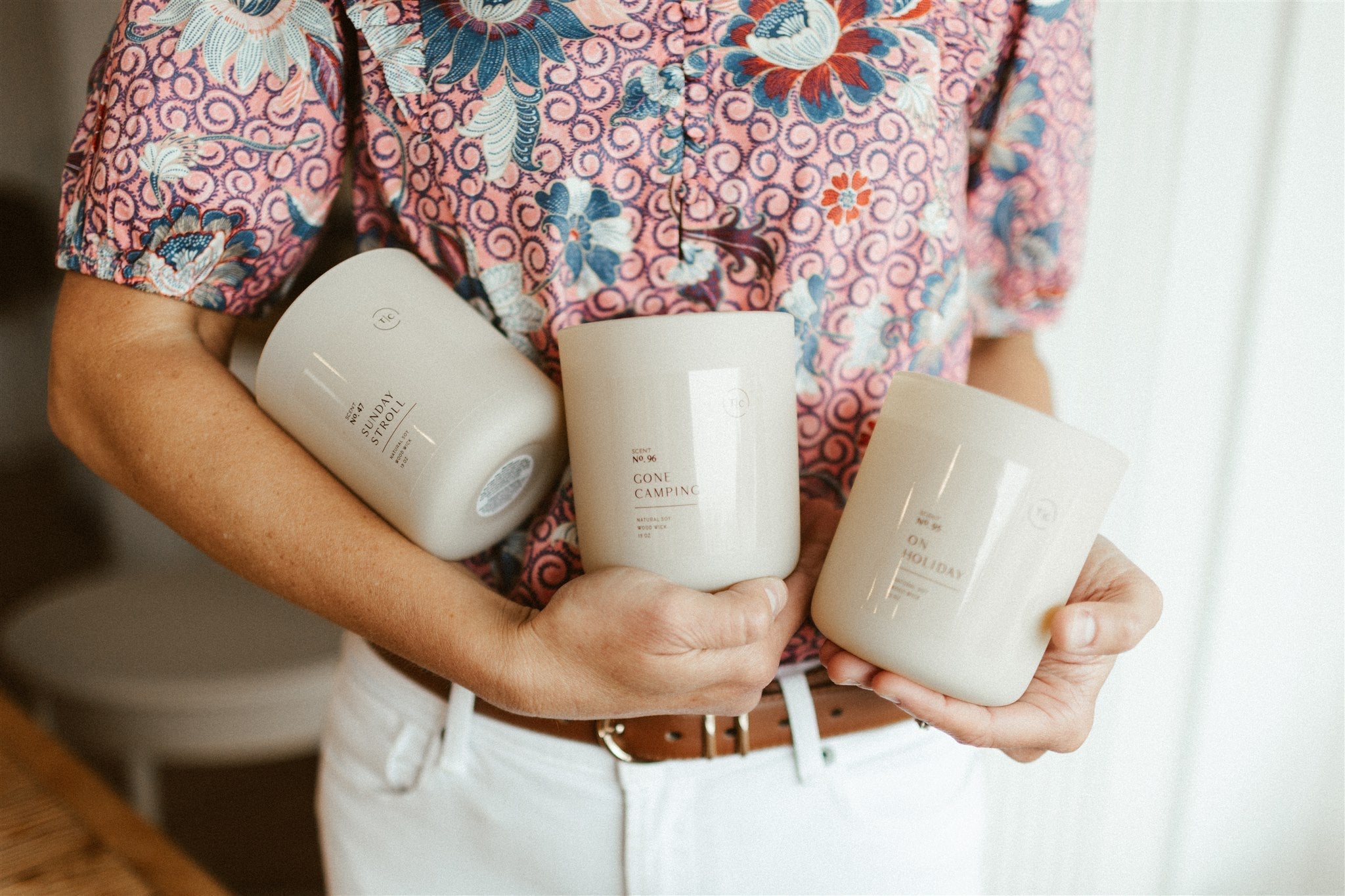 Spring and summer candles in cream vessels surrounded by lilac trimmings, watermelon slice, and cucumber.